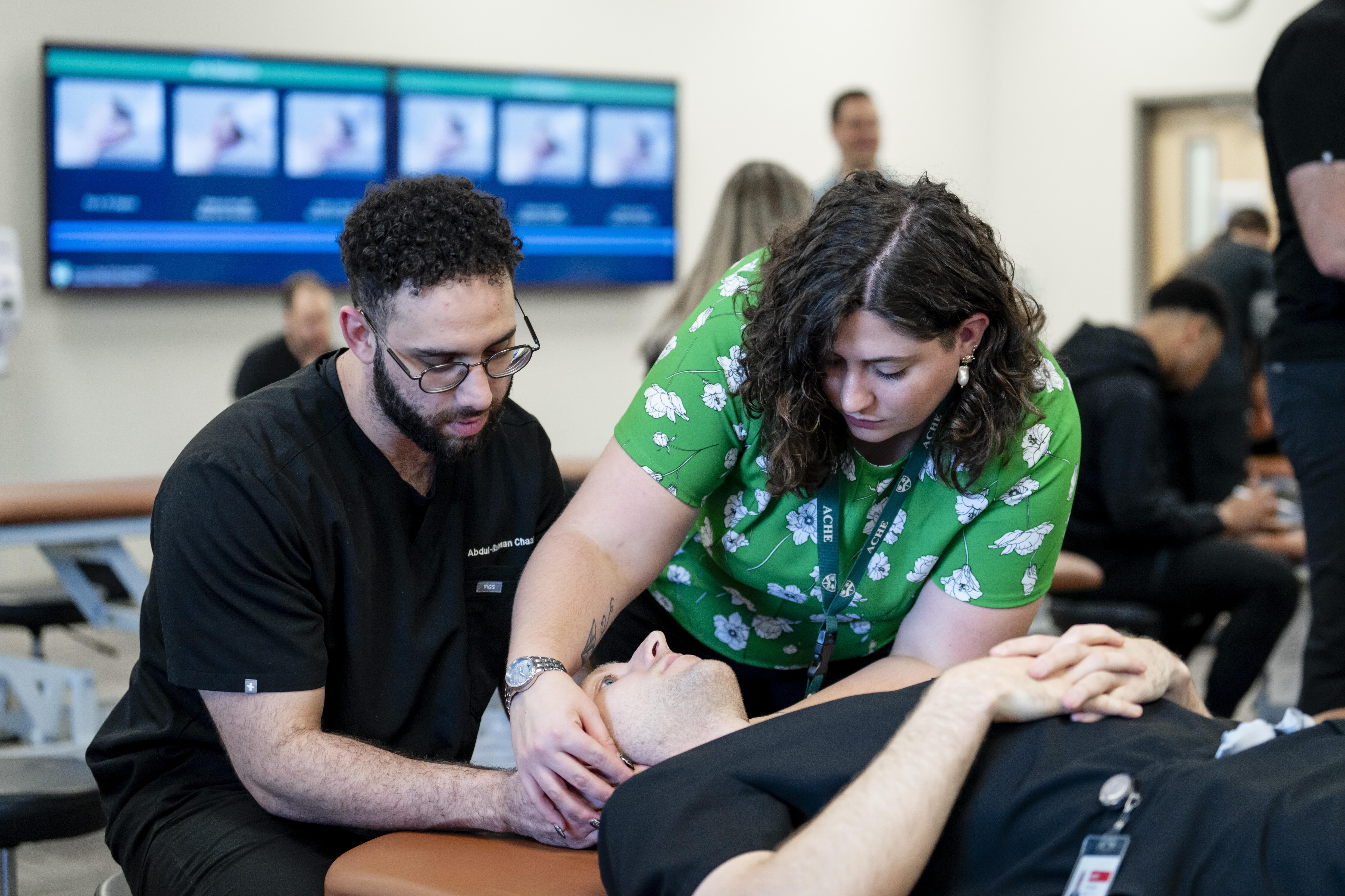 Two people evaluating a patients neck and head while the patient is laying down at Arkansas College of Osteopathic Medicine.