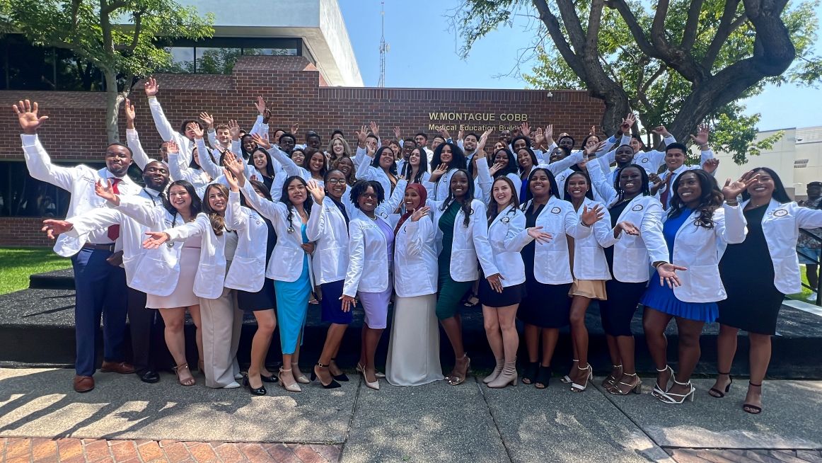 Large group of students at Charles R. Drew University of Medicine and Science standing in their white coats cheering.