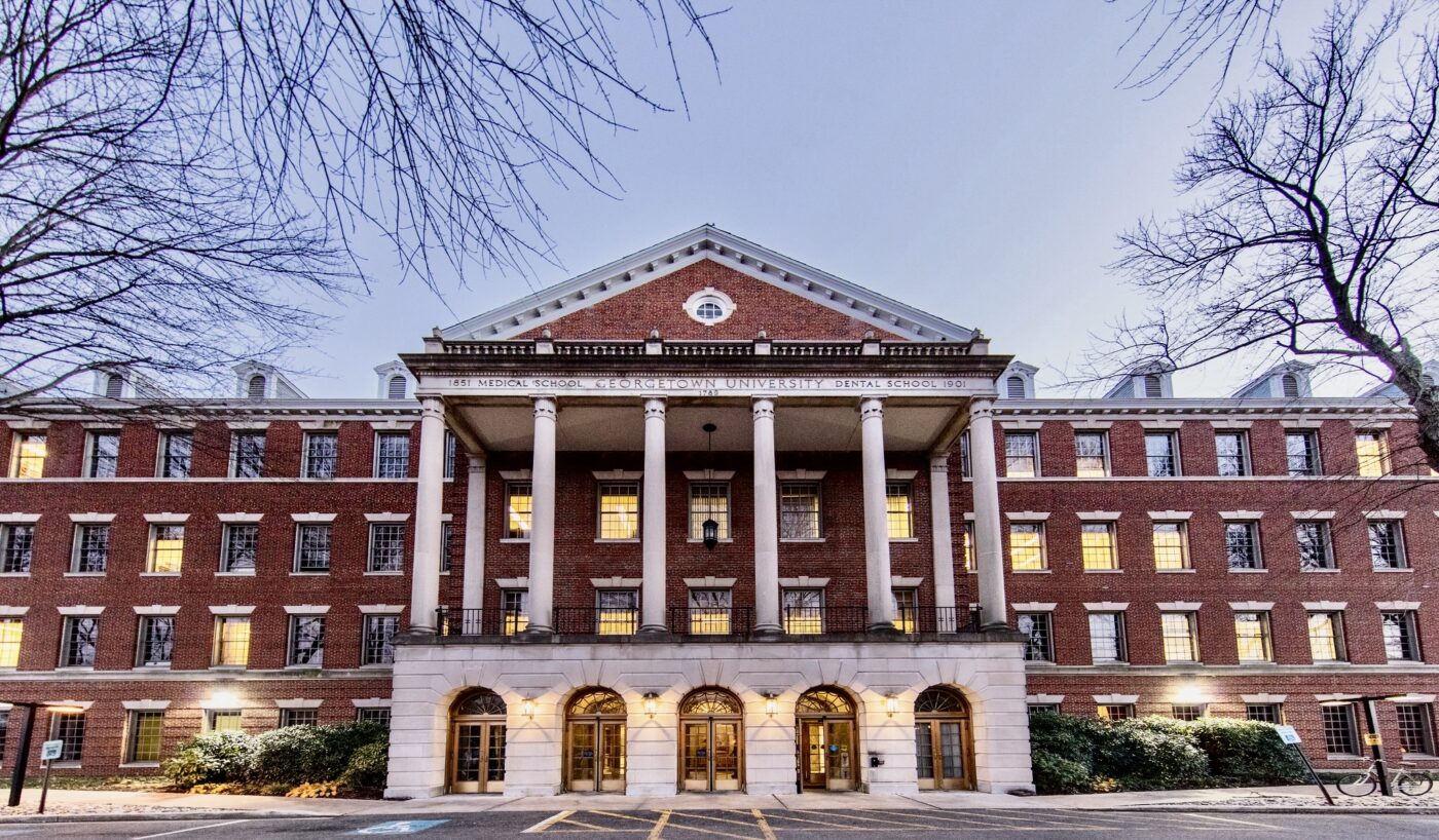 Historic brick building with large columns and a symmetrical façade, surrounded by leafless trees.