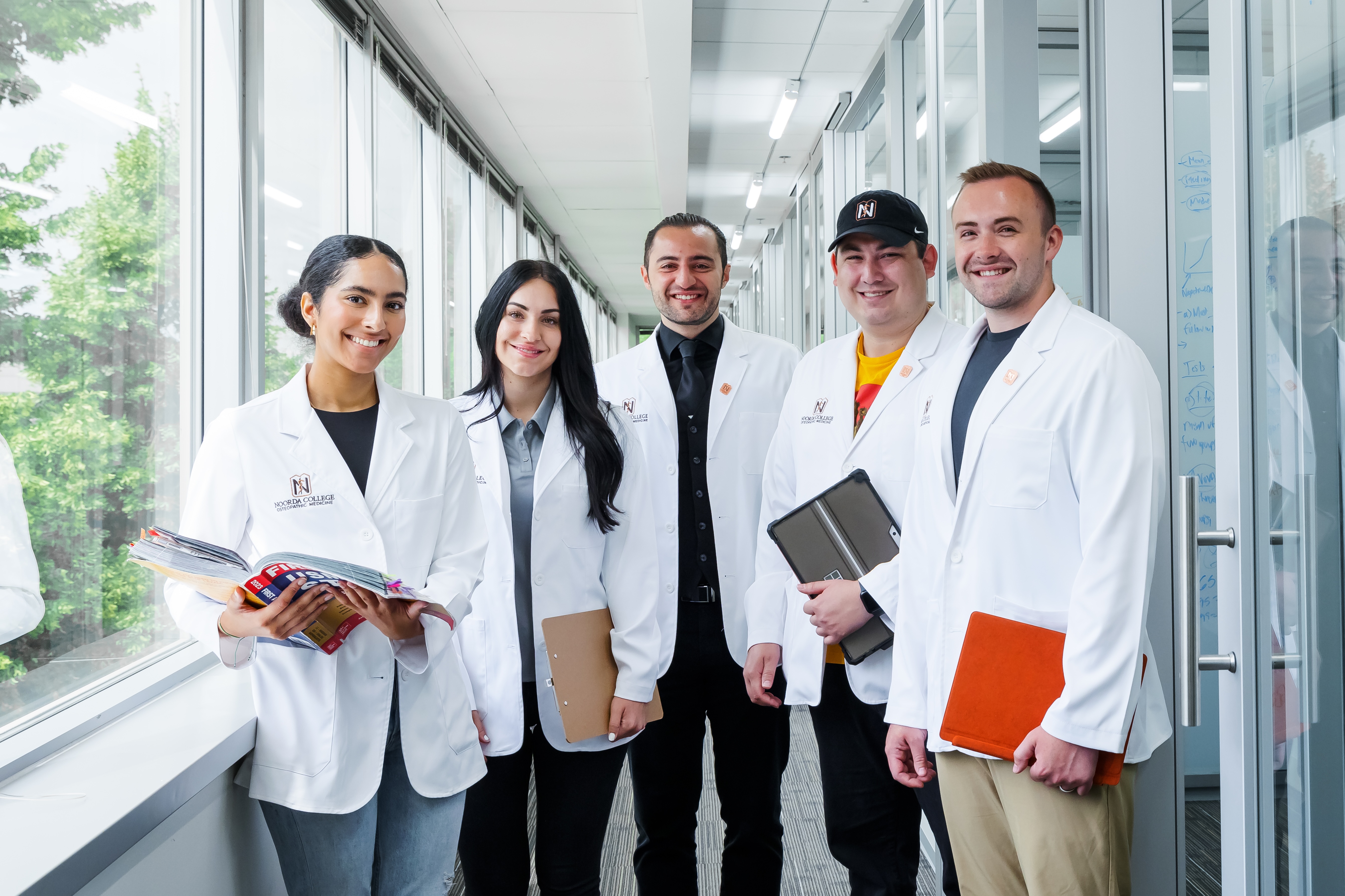 Five students in the Noorda College of Osteopathic Medicine program smiling at the camera while holding various school related items.
