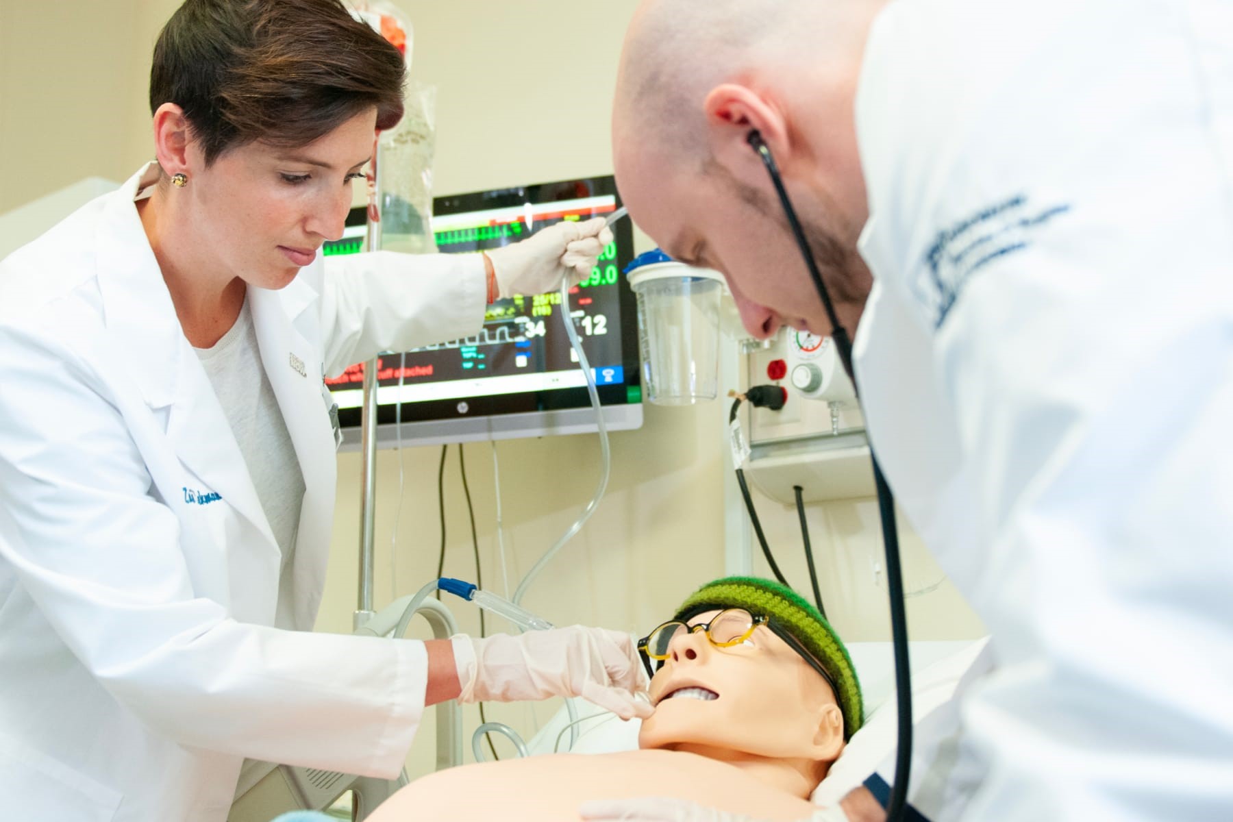 One student suctioning the mouth of a patient while another student listens to the patients heart beat.