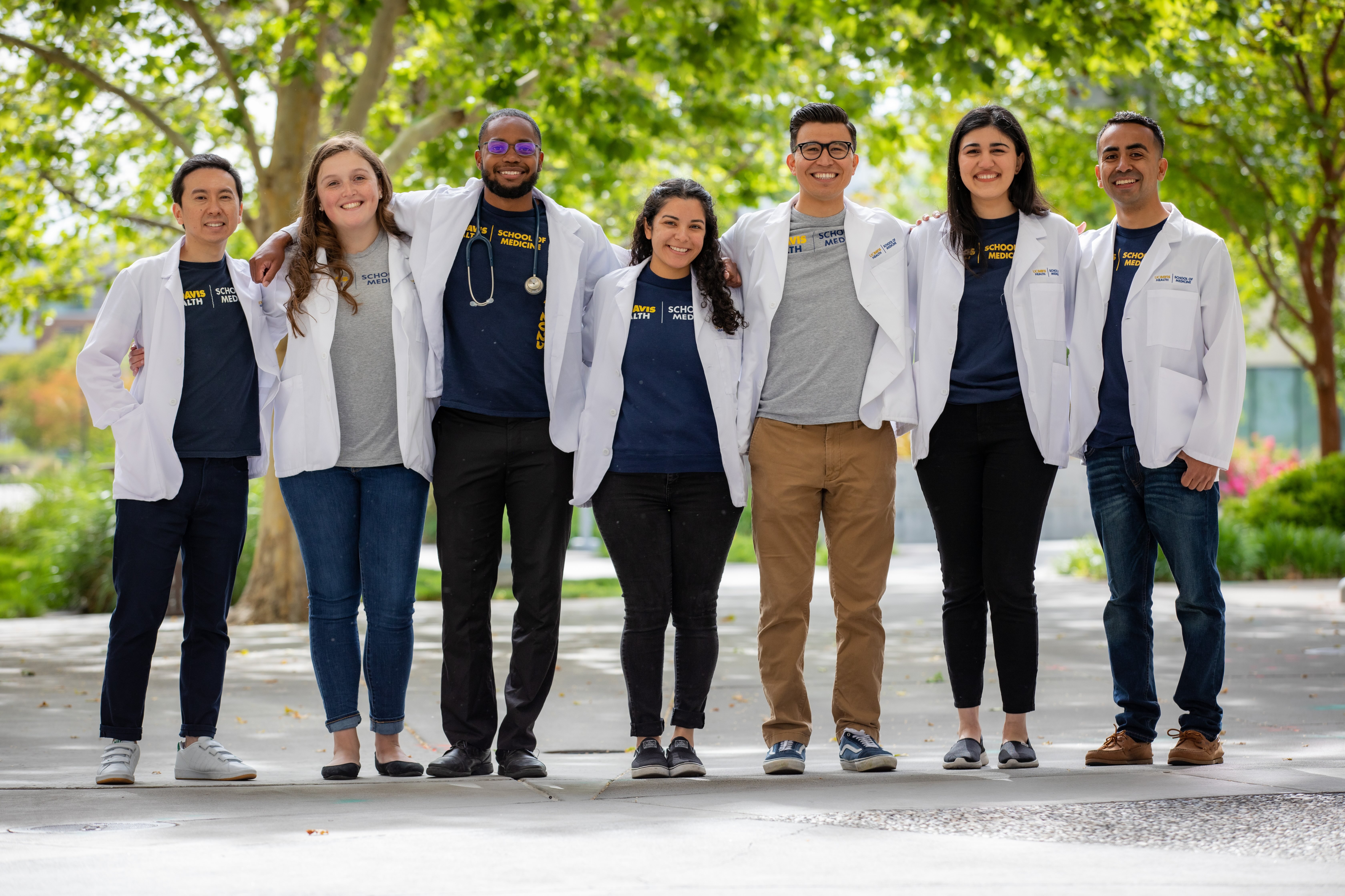 Small group of student posing for a photo wearing UC Davis School of Medicine shirts and white coats.