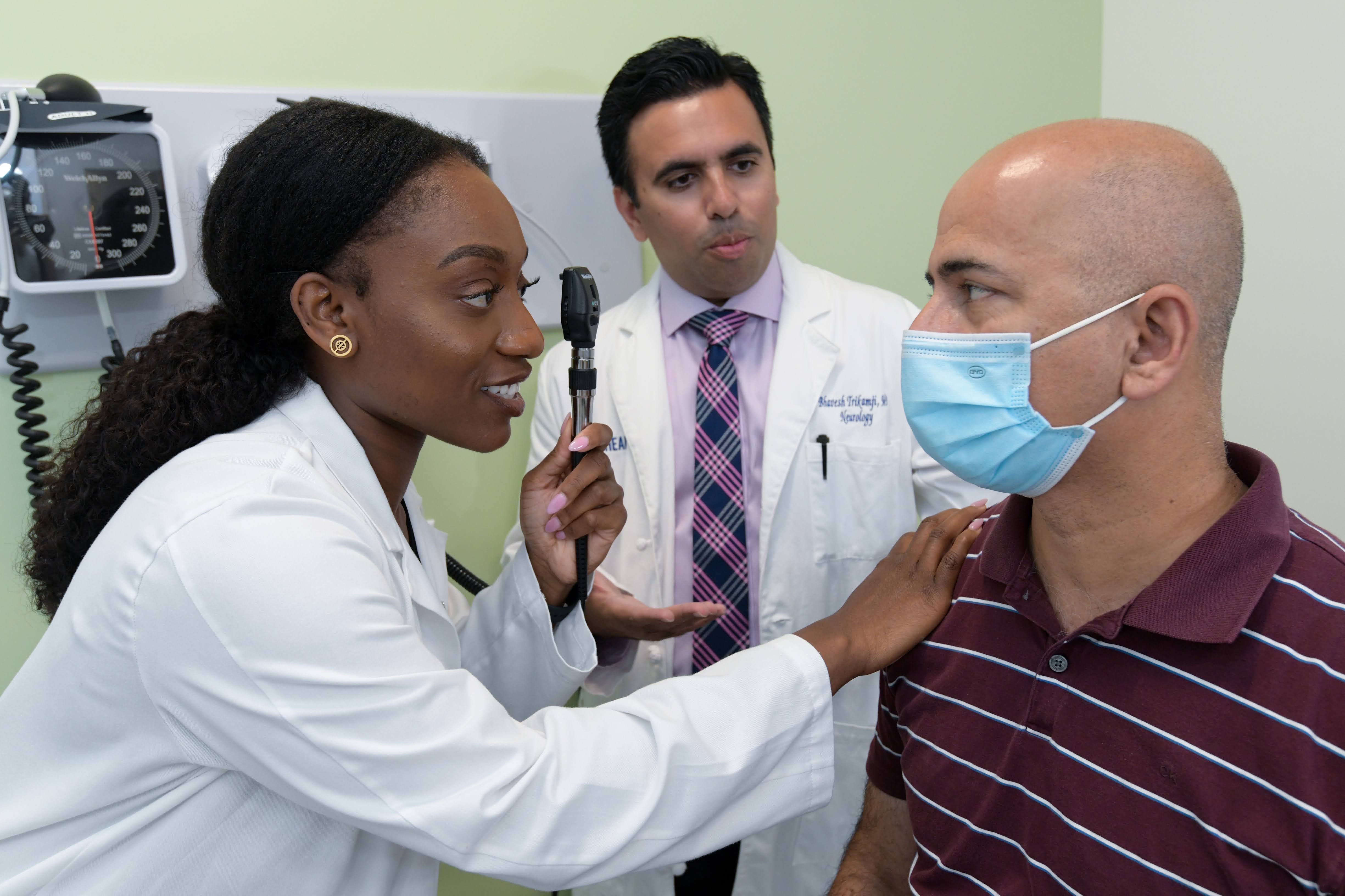 Student in the UCR SOM doing an eye exam on a patient while another student observes.