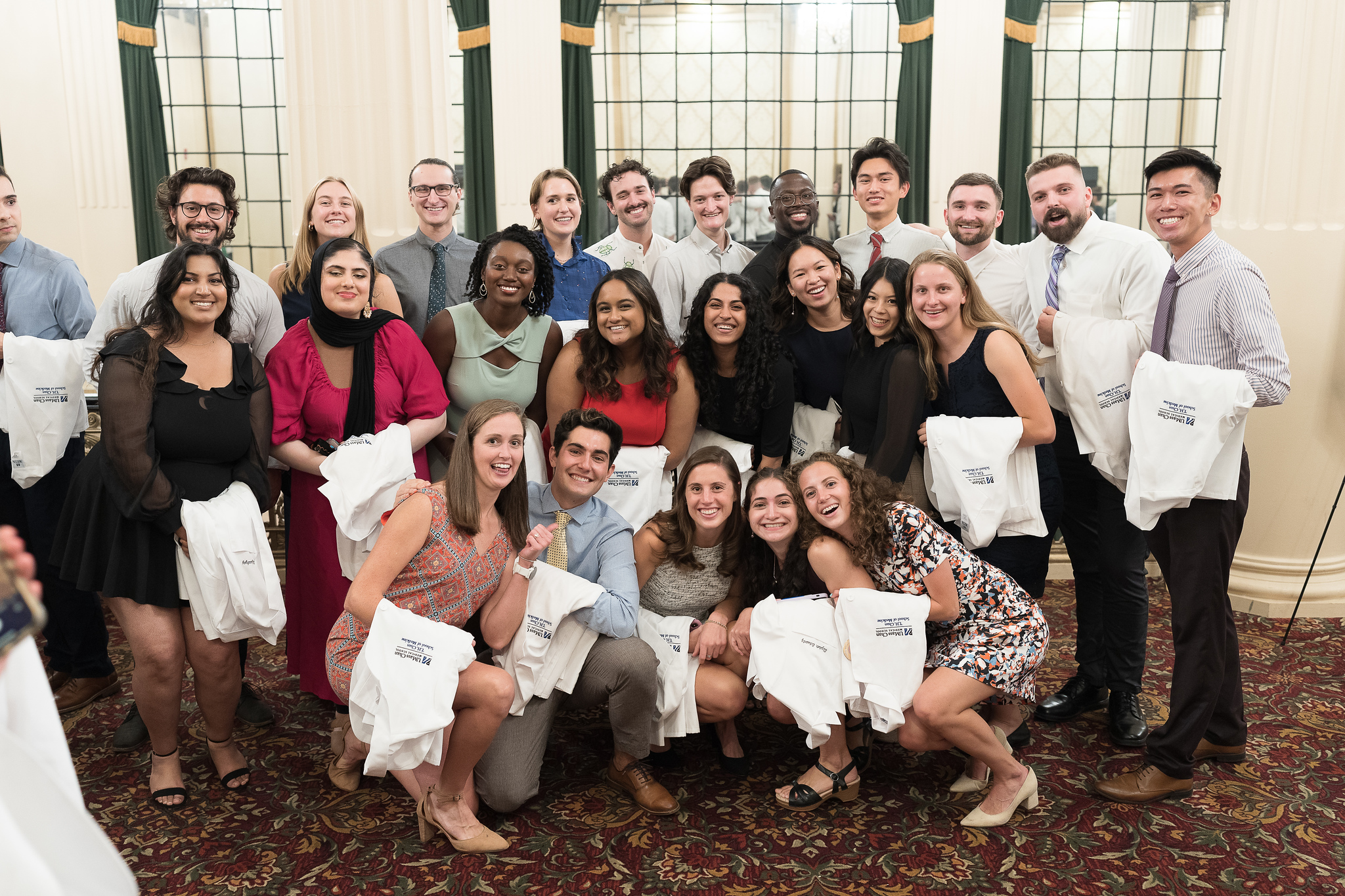 Group of students that attend UMass smiling at the camera holding their white coats.