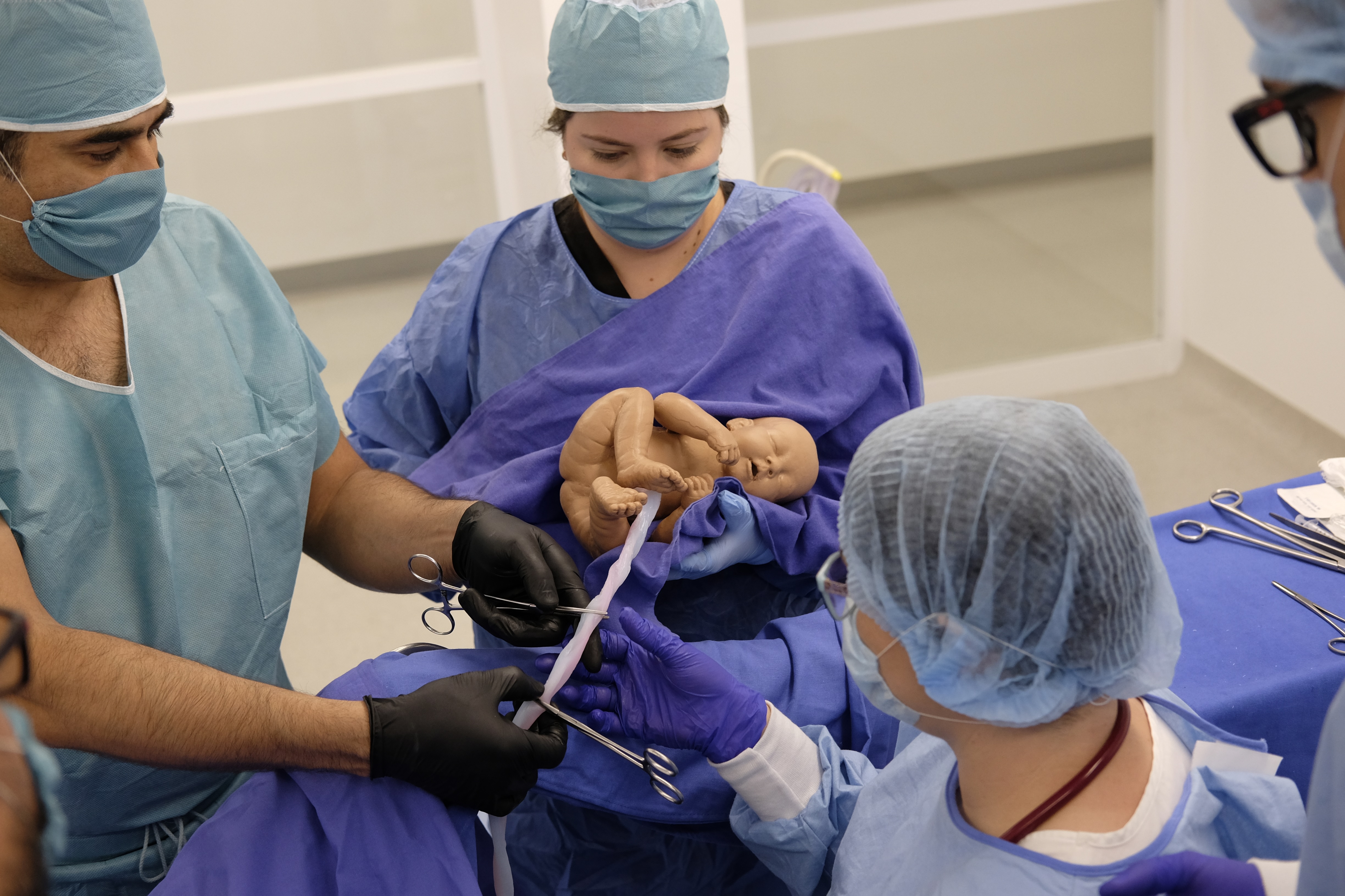 Students in action practicing cutting the umbilical cord on a medical manikin after a birth.