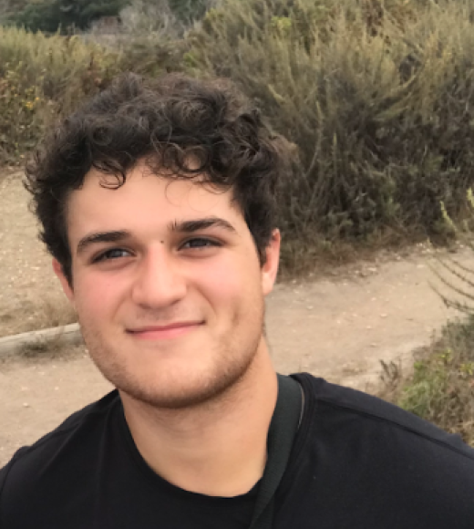 A picture of Christian standing on a hill with greenery in the background.